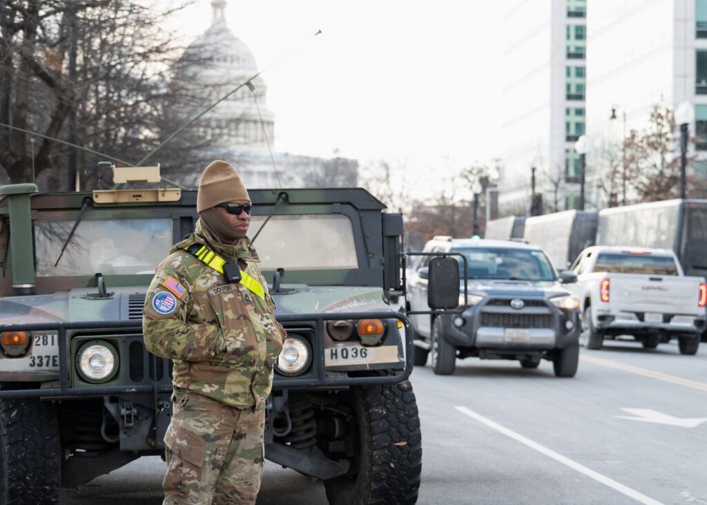 A National Guard soldier stands watch in Washington, D.C., beside a military Humvee with the Capitol behind.